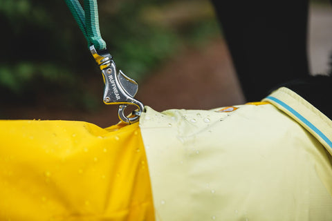 Close-up of a Ruffwear, Sun Shower Jacket, Mineral Yellow with a metal clip on a blurred background