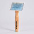 An ARTERO pet grooming brush with a light-colored wooden handle and a metal head featuring a light blue protective cover and silver pins, shown on a solid white background.