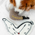Dog playing with a heart-shaped pillow on a blanket with a clock design