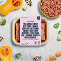 Naturaw pet food packaging with ingredients listed on a gray surface with food items around.