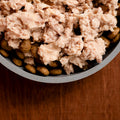 Dog food with meat chunks and kibble in a bowl on a wooden surface