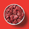 White bowl filled with raw beef chunks on a red background