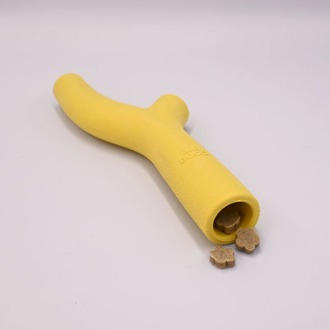 Yellow dog toy with treats on a light Grey background.