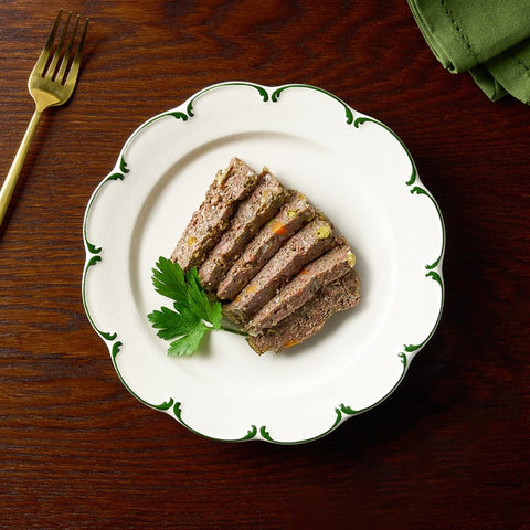 Three slices of meatloaf on a decorative white plate with green trim, served on a wooden table.