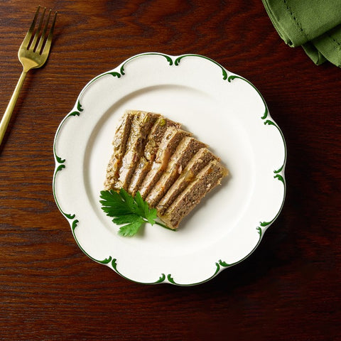 Sliced meat dish on a decorative plate with a fork and green napkin on a wooden table.