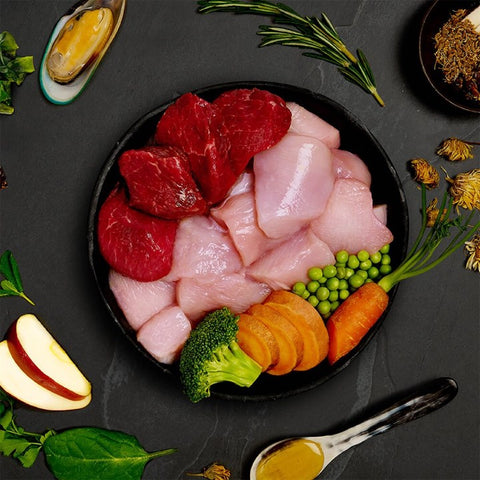 Assorted raw meats and vegetables on a dark surface with herbs and spices.