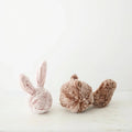 Two plush toys, one pink bunny and one brown squirrel, on a light wooden surface with a white background.