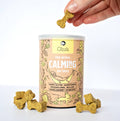 Gizzl's calming dog treats with a hand holding a treat above the container on a white background
