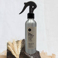 Silver spray bottle with black nozzle on a stone surface with wheat stalks, against a light background