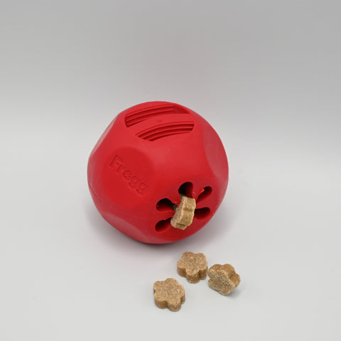 Red dog toy with a central hole and three treats on a light neutral background.