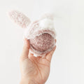 Hand holding a pink bunny-shaped dog Toy with a ball inside against a white background