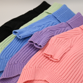 Row of colorful ribbed knit sweaters on a light background