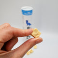 Hand holding a small square fish treat with a container in the background
