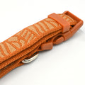 Close-up of an orange woven strap with a matching orange plastic buckle and a silver metal ring, shown on a white background.