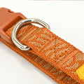 Close-up of an orange woven dog collar with a silver metal D-ring and a brown plastic buckle, shown on a white background.