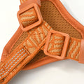 Close-up of an orange woven pet harness with adjustable plastic buckles and a breathable mesh backing, shown on a white background.
